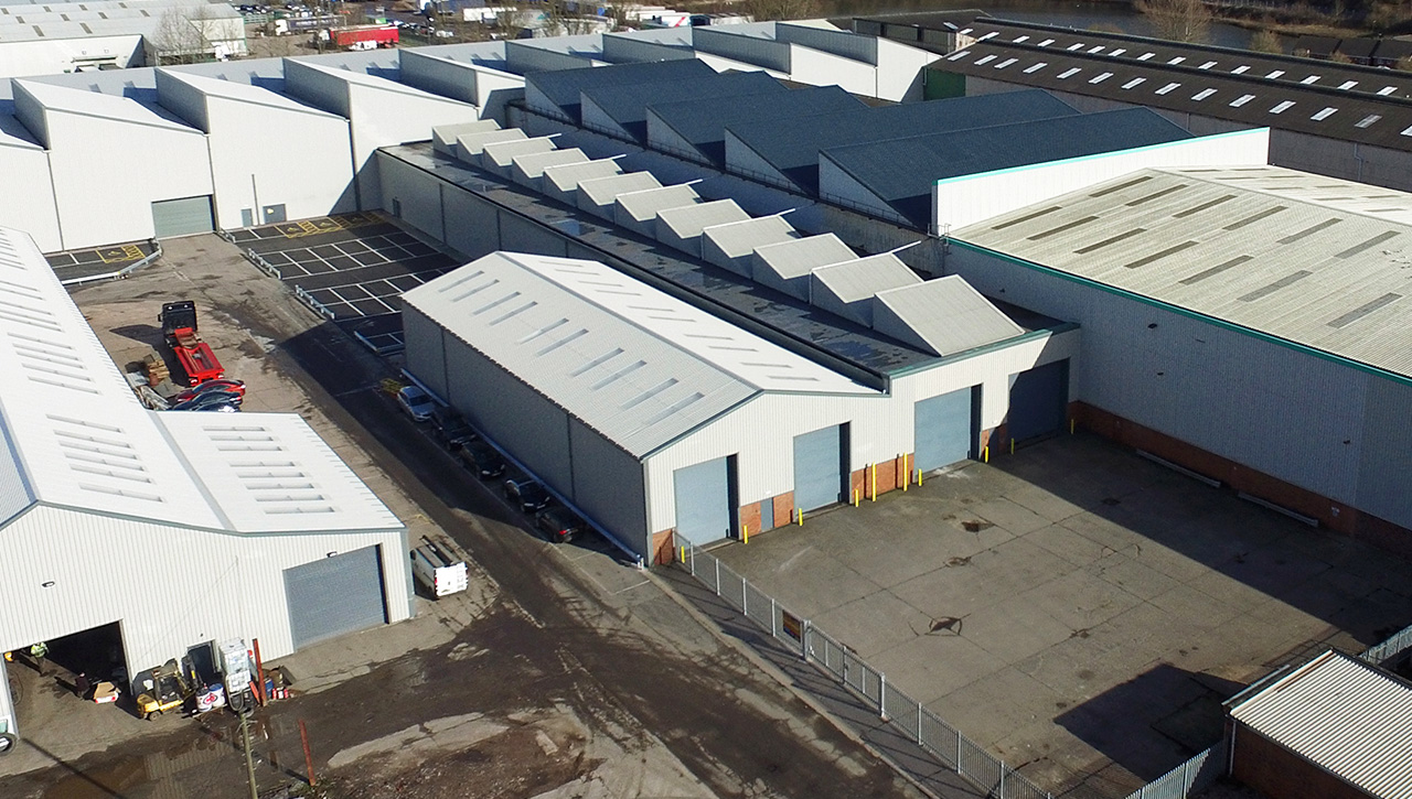 Aerial view of several industrial warehouses with white roofs, adjacent parking areas, and surrounding paved surfaces.
