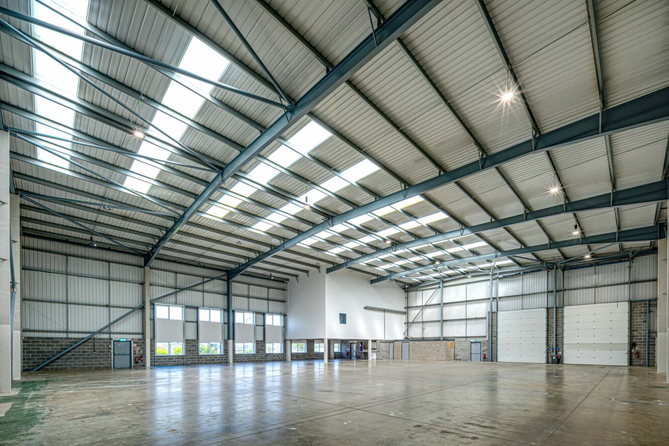 Interior of a large empty warehouse featuring high ceilings, skylights, and concrete flooring with loading bay doors on one side.