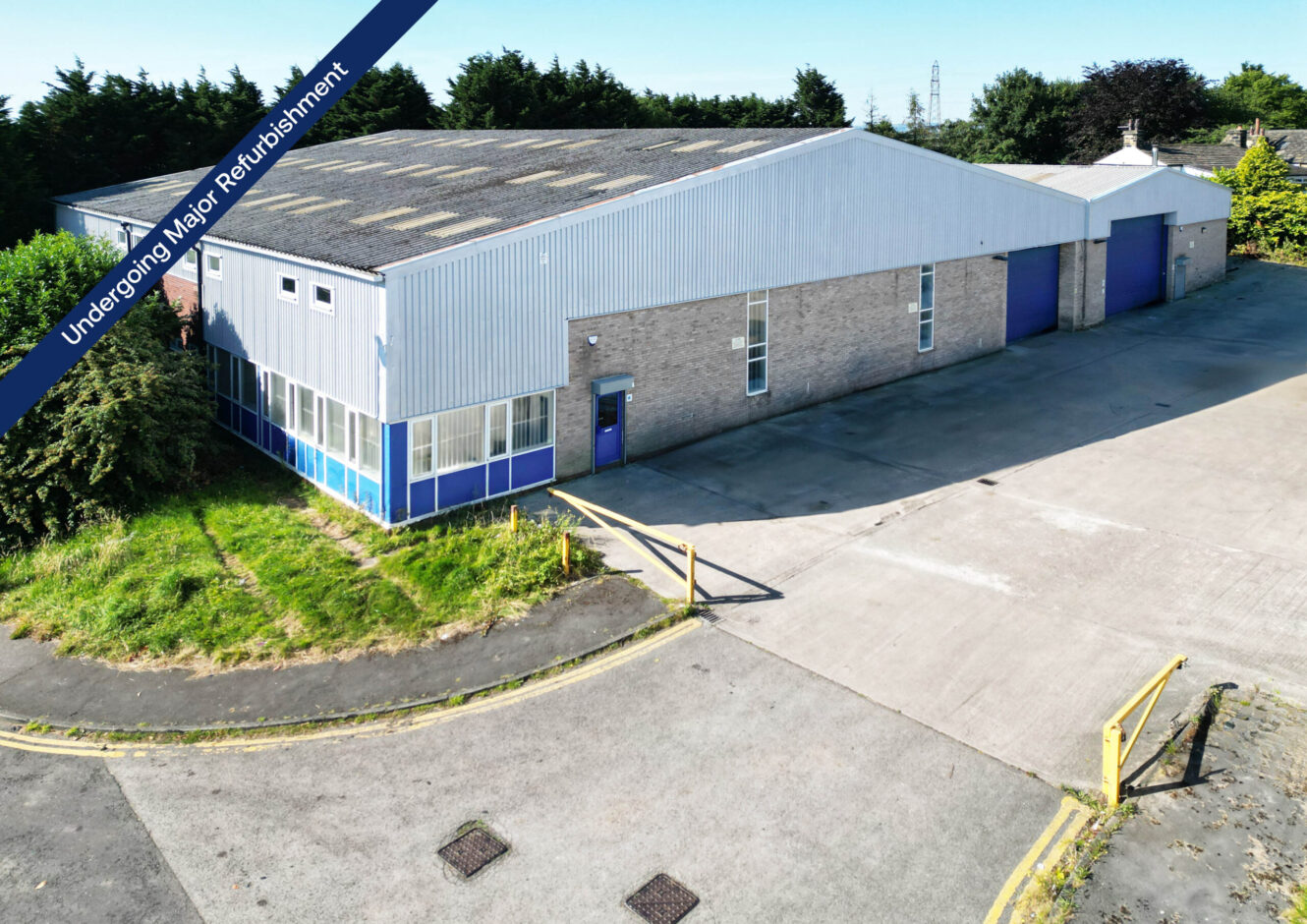 A large industrial warehouse with a brick and metal exterior, blue doors, and windows, shown with a banner reading “Undergoing Major Refurbishment”.