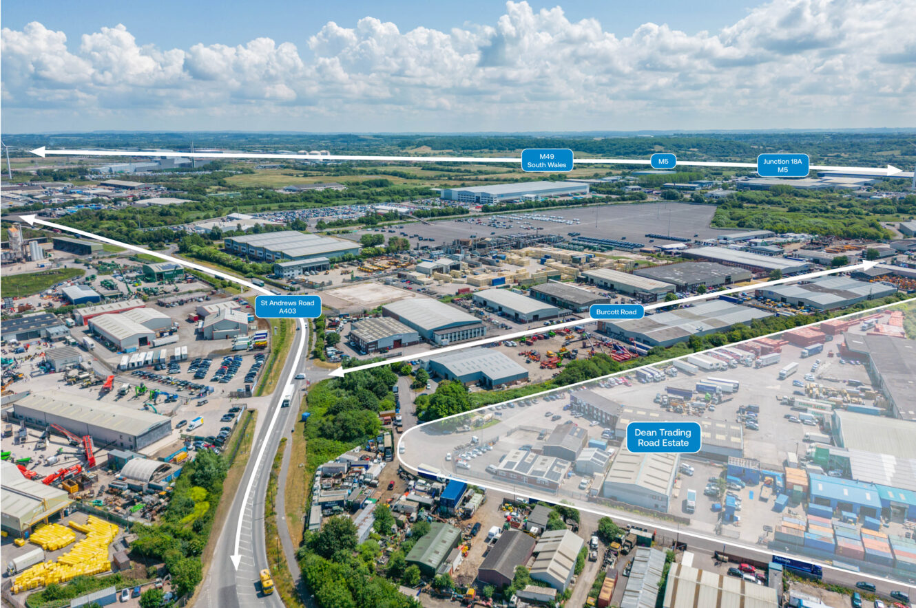 Aerial view of an industrial estate with several labelled roads, warehouses, and buildings, surrounded by greenery under a partly cloudy sky.