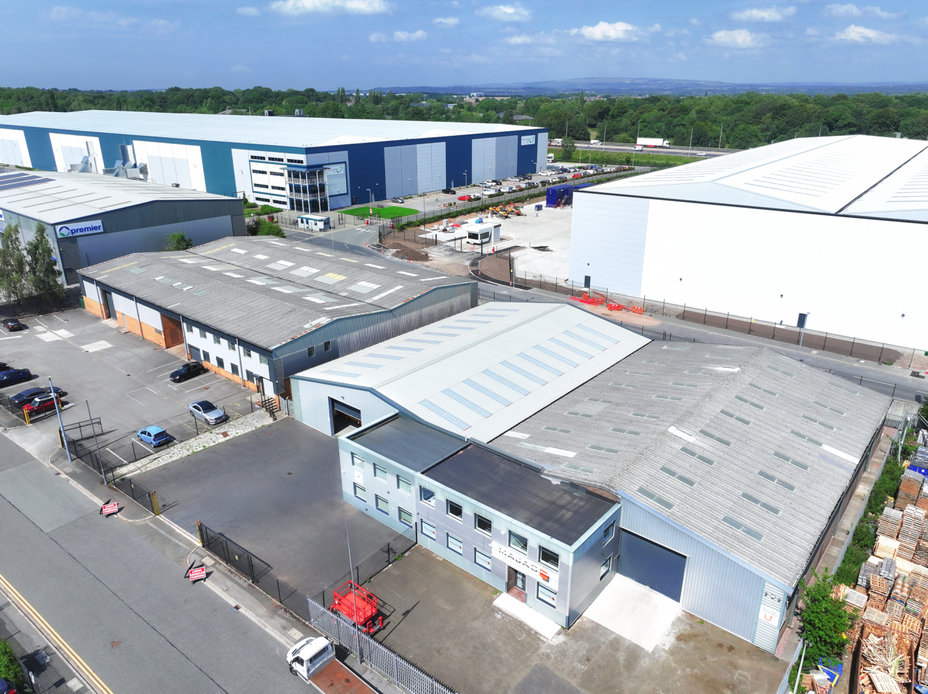 Aerial view of an industrial estate with several large warehouse buildings, car parks, and surrounding roads on a clear day.