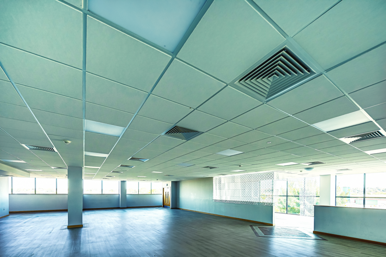 Spacious, empty room with a tiled ceiling, large windows on two sides, and sunlight streaming in onto the wooden floor.