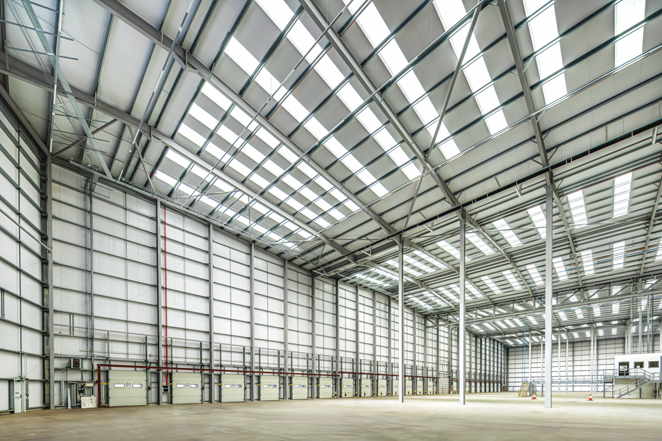 Spacious, empty industrial warehouse interior with high ceilings, large skylights, and multiple loading bay doors along one wall.
