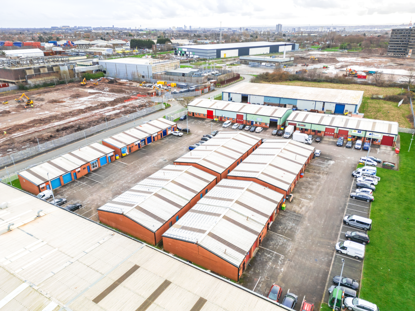 Aerial view of an industrial estate with rows of warehouses, parked vehicles, and adjacent building site.