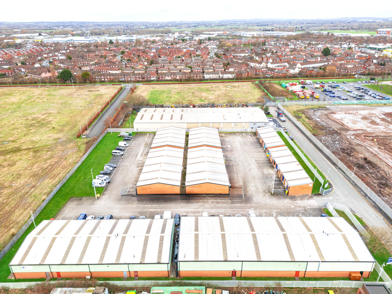 Aerial view of a storage facility with multiple large warehouse units, parking areas, and adjacent residential neighbourhood in the background.