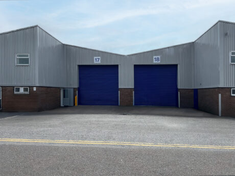 Two industrial warehouse units with blue roller shutters numbered 17 and 18, set in a brick and metal building under a cloudy sky.