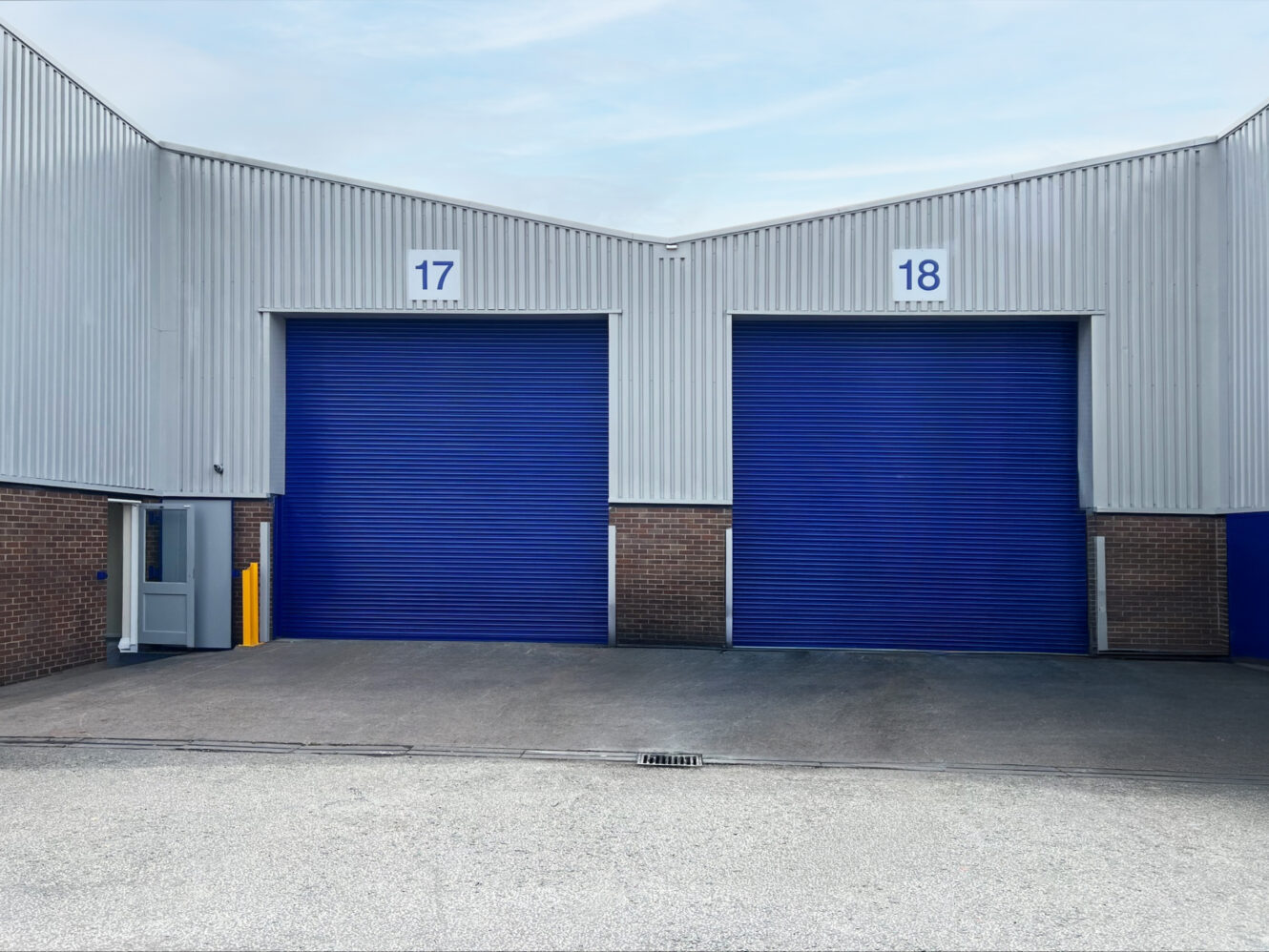 Two industrial warehouse units with blue roller shutters numbered 17 and 18, set in a metal and brick building with a paved forecourt.