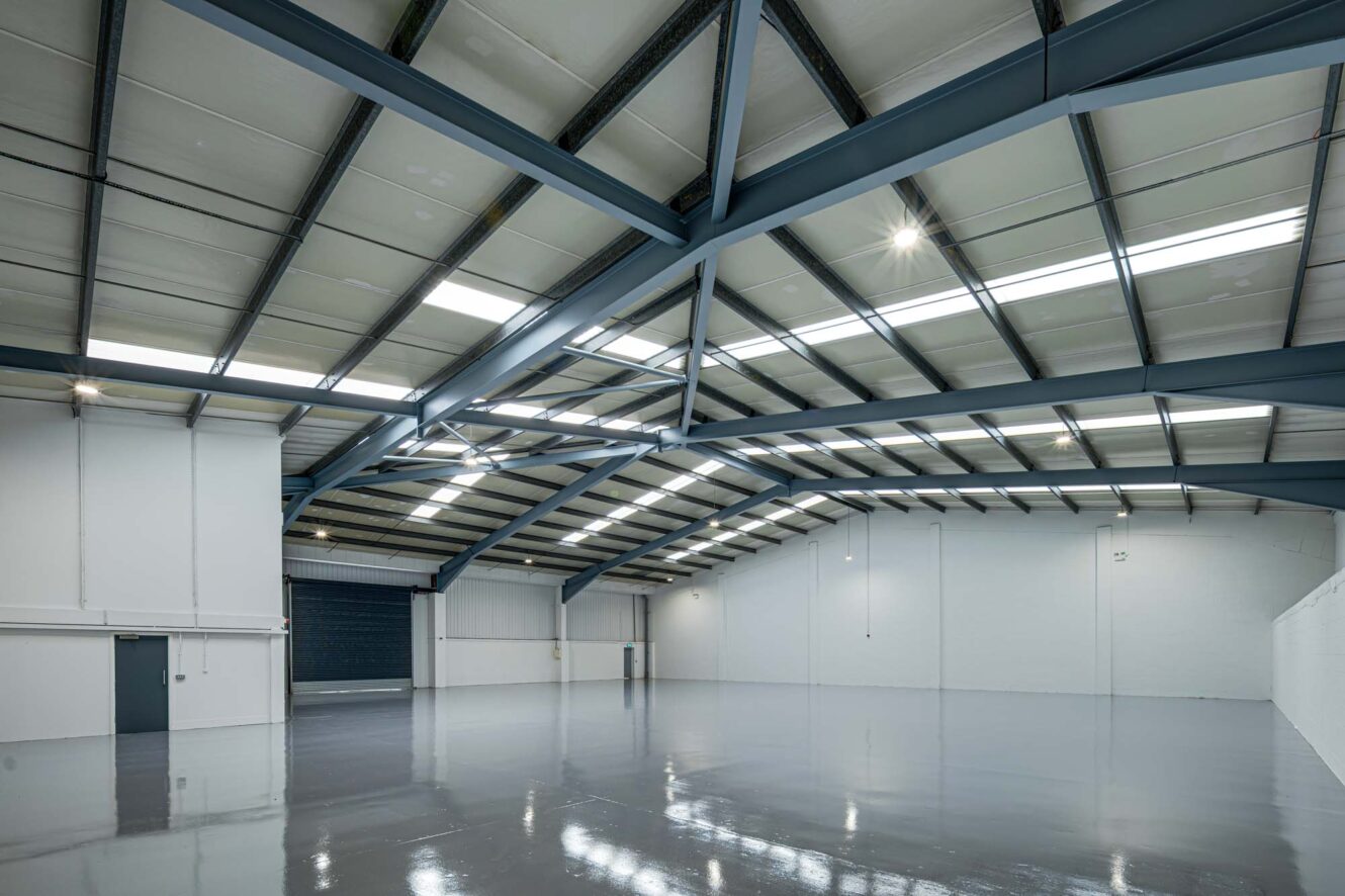 Interior of a large empty warehouse with polished concrete floor, high ceiling, exposed steel beams, and white walls.