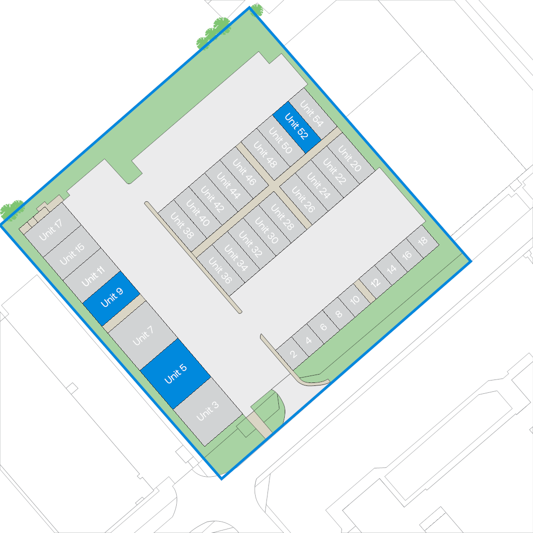 Site plan of a building complex showing labelled units in grey and blue, bordered by green areas, with pathways and parking spaces visible throughout the layout.