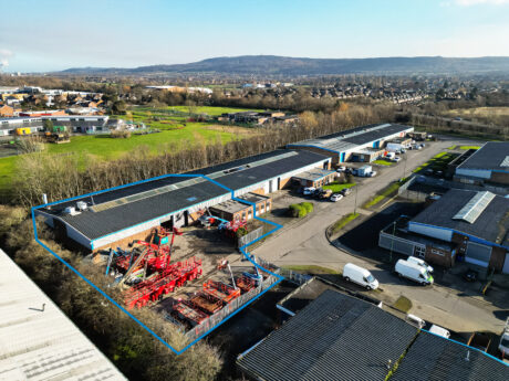 Aerial view of an industrial estate with warehouses and parked vehicles; one lot outlined in blue contains construction equipment and materials.