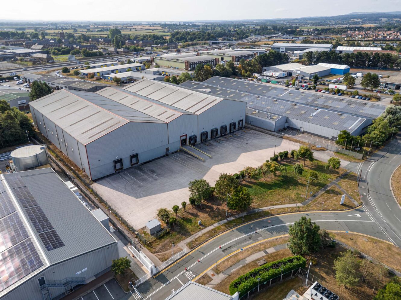 Aerial view of a large industrial warehouse with multiple loading bays, surrounded by other commercial buildings and greenery.