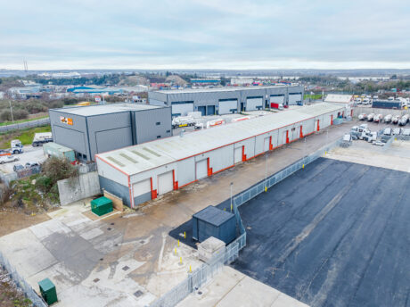 Aerial view of an industrial complex with warehouses, parked lorries, and loading bays on a cloudy day.