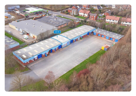 Aerial view of a commercial warehouse complex with multiple units; one unit labelled “Unit 85” is highlighted in blue. Nearby are buildings, houses, trees, and a parking area.