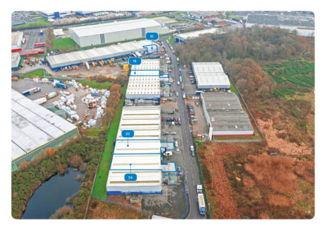 Aerial view of an industrial estate with numbered warehouse units, parking areas, adjacent road, and surrounding greenery.