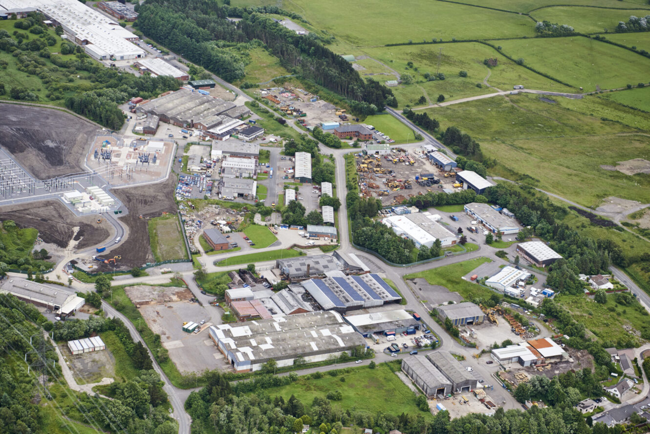 Aerial view of an industrial estate with multiple warehouses and buildings surrounded by fields, roads, and greenery.