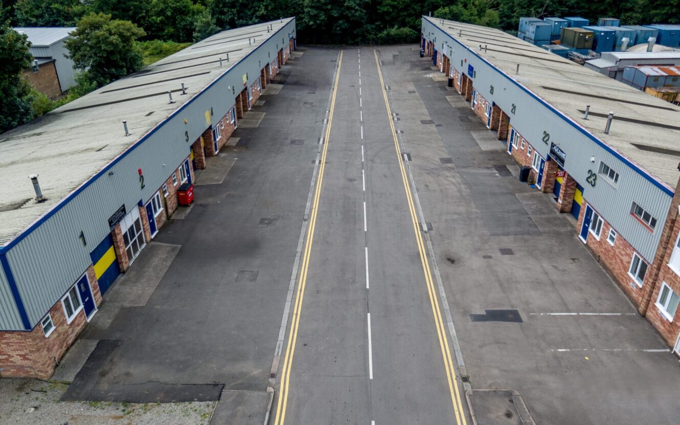 Aerial view of an empty street between two rows of industrial warehouse units with closed blue doors and brick façades.