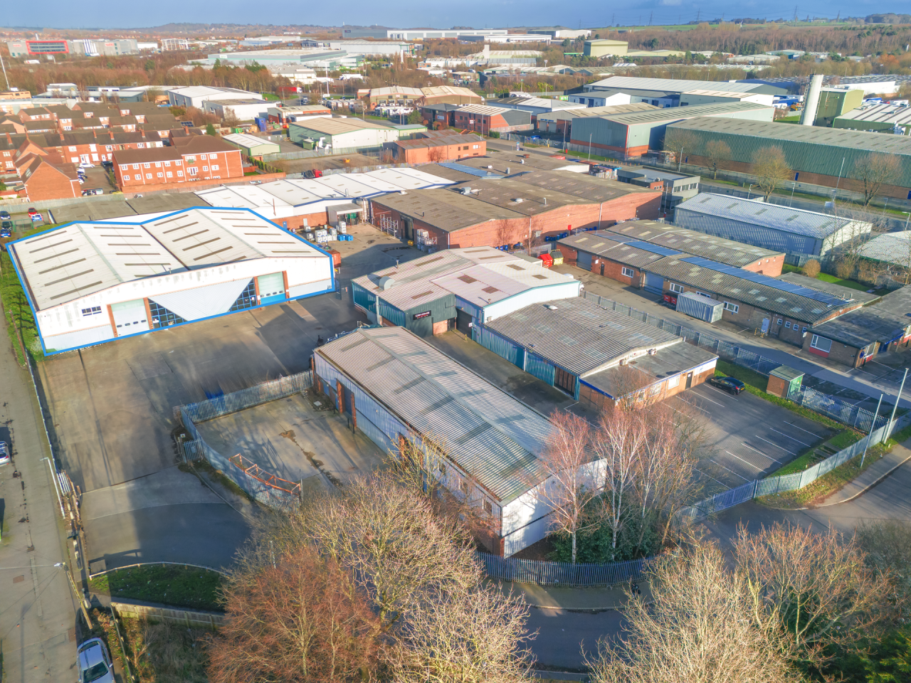 Aerial view of an industrial area with multiple warehouses and factories, surrounded by roads and scattered trees, under a clear sky.