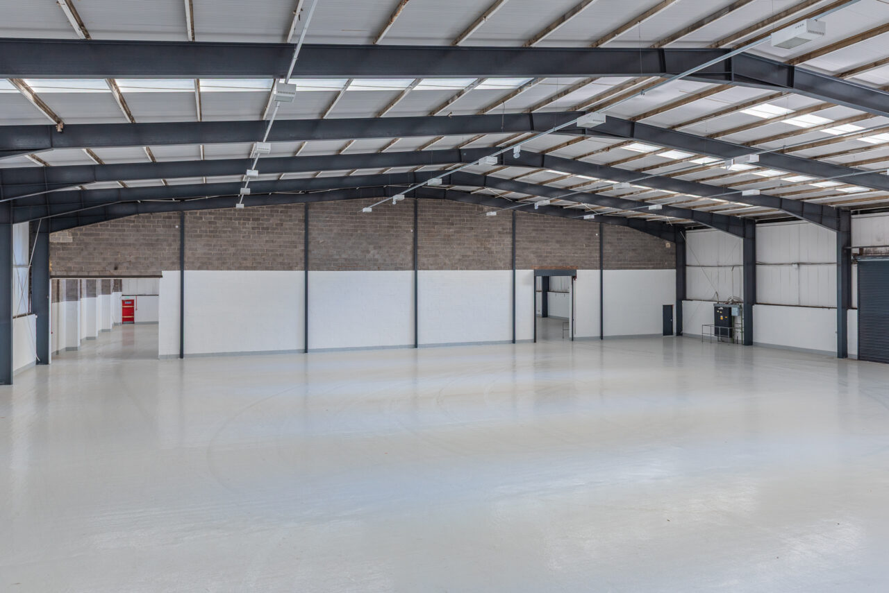 Interior of a large, empty warehouse with a polished concrete floor, high ceiling, exposed steel beams, and white partition walls.