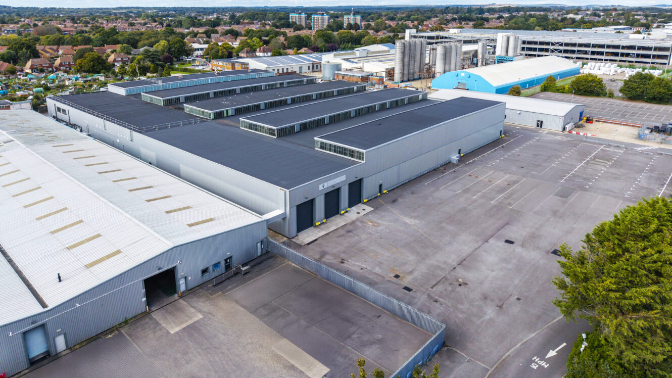 Aerial view of a large industrial warehouse complex with multiple buildings, parking areas, and adjacent industrial facilities in a suburban setting.