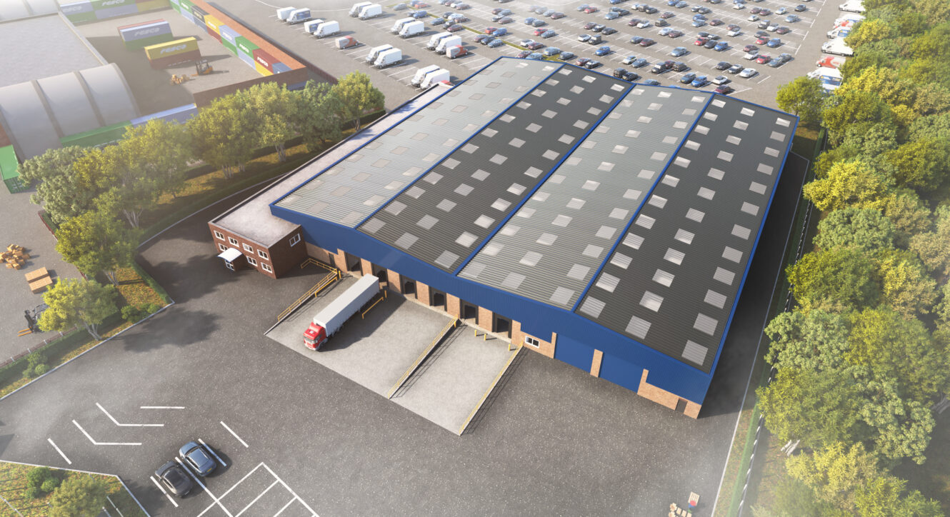 Aerial view of a large warehouse with a lorry at the loading bay, surrounded by car parks, trees, and adjacent parked vehicles.
