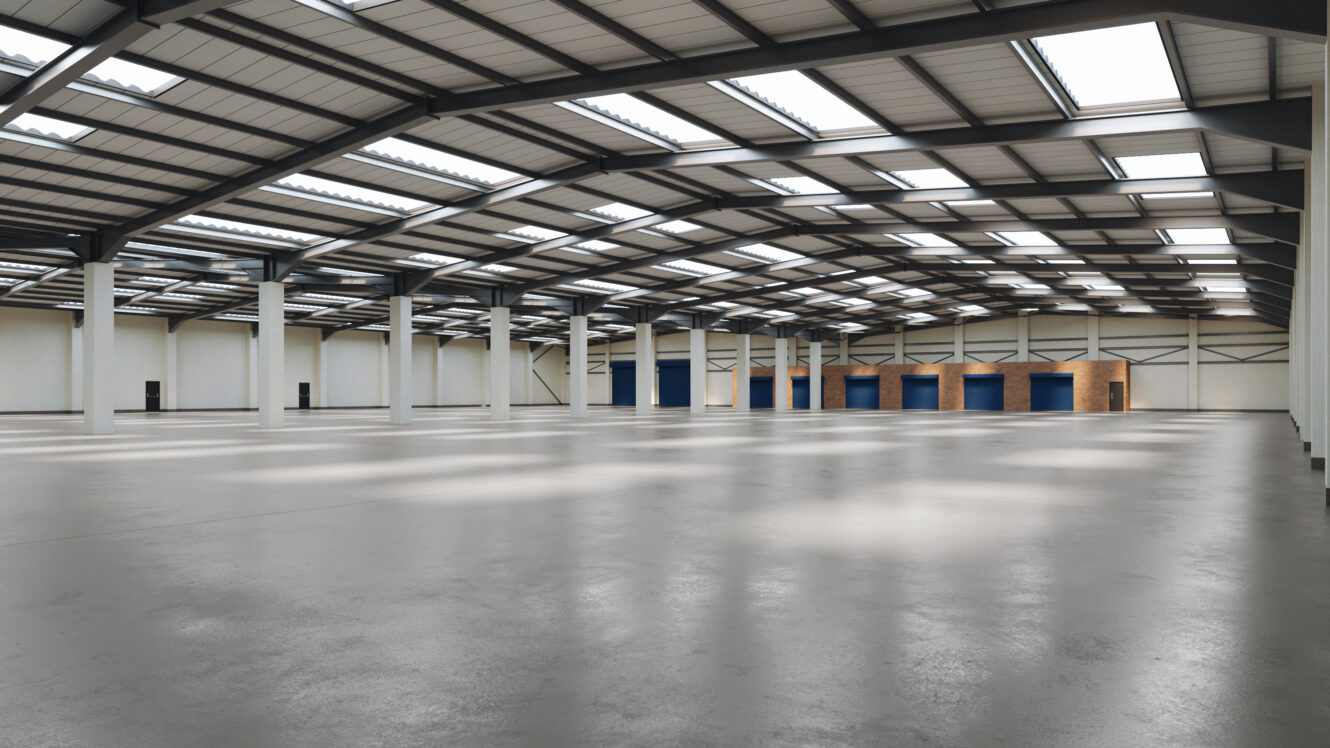 A large, empty warehouse with high ceilings, multiple skylights, and several loading bays along one wall.