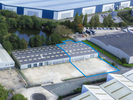 Aerial view of an industrial warehouse building with a blue outline marking a section of the property, surrounded by car parks and greenery.
