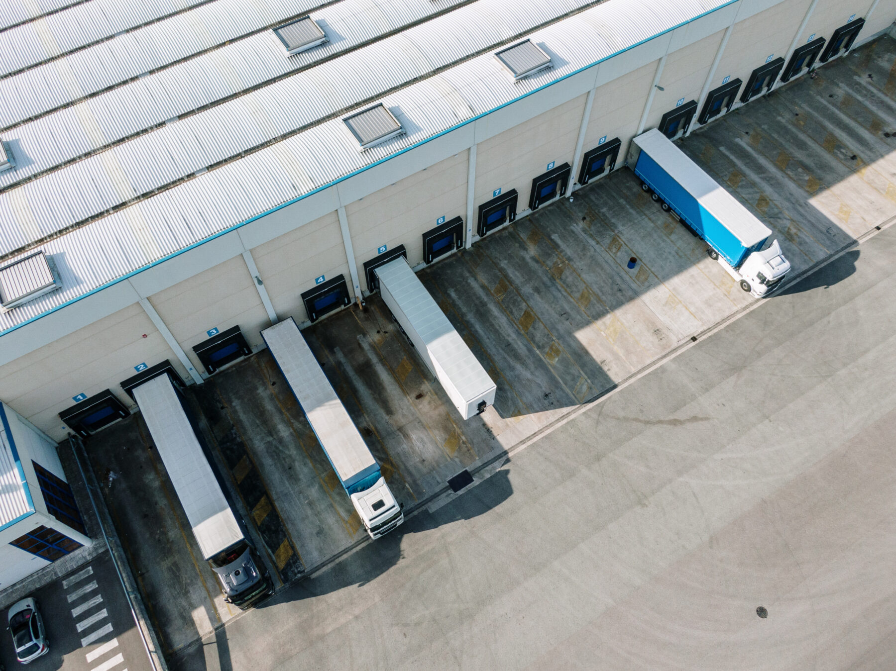 Aerial view of a warehouse loading bay with several lorries parked at different bays, some loading or unloading, and one bay empty.