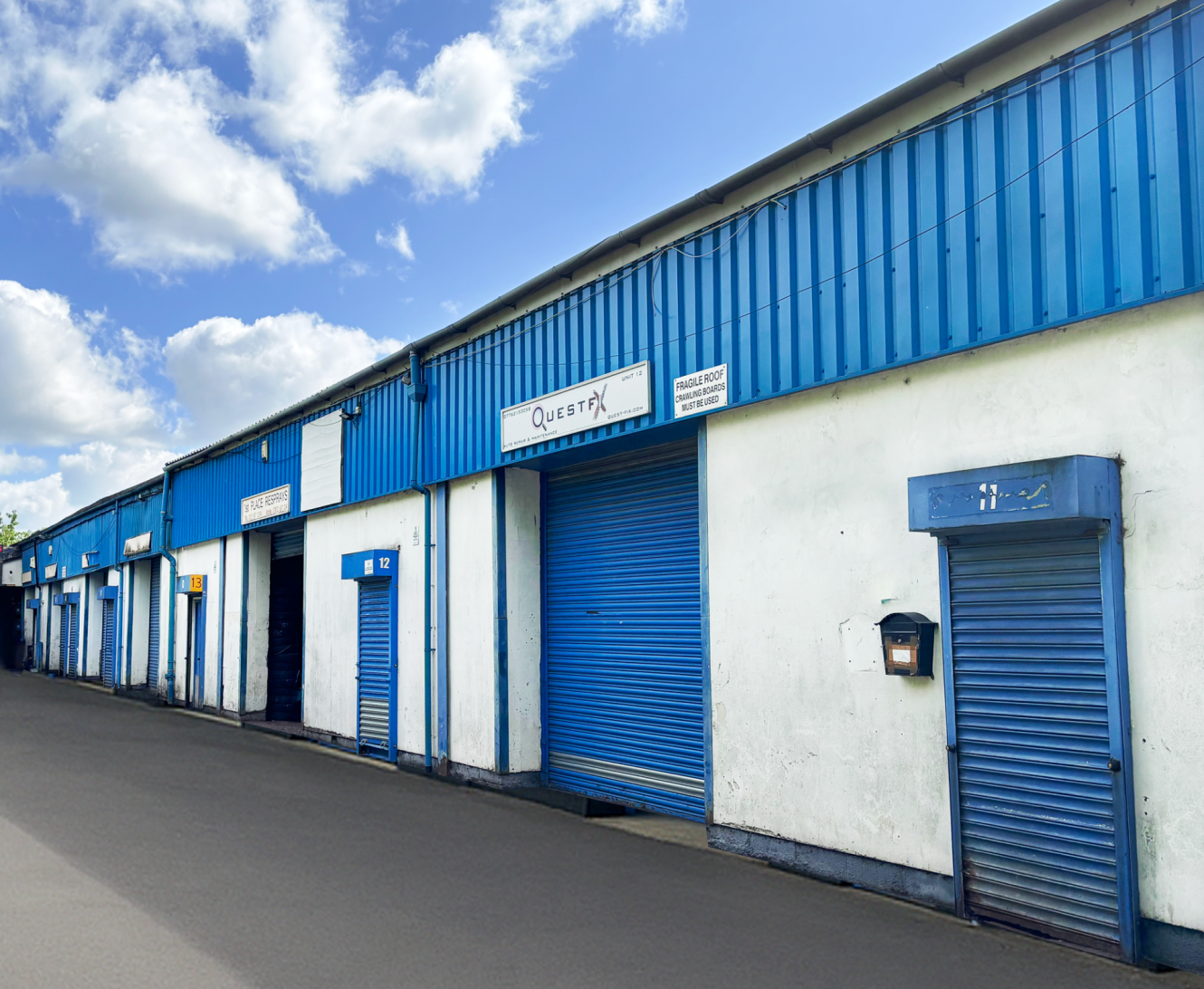 Blue and white industrial storage units with closed roller shutter doors beneath a partly cloudy sky. A Questax sign is above one door.