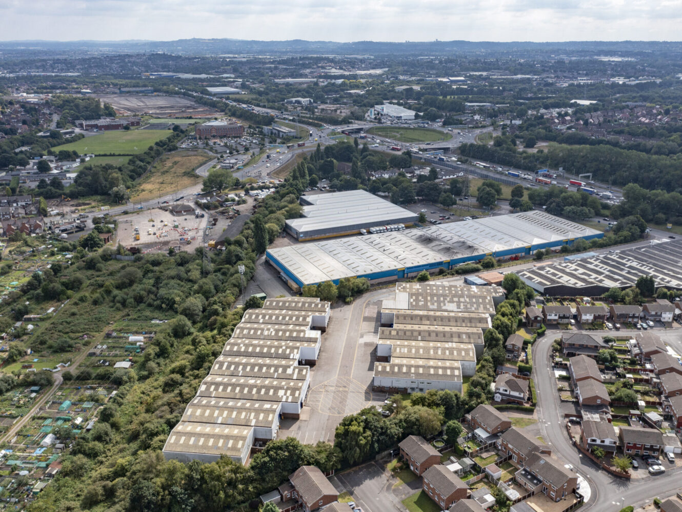 Aerial view of an industrial estate with warehouses, bordered by houses, allotments, and major roads.