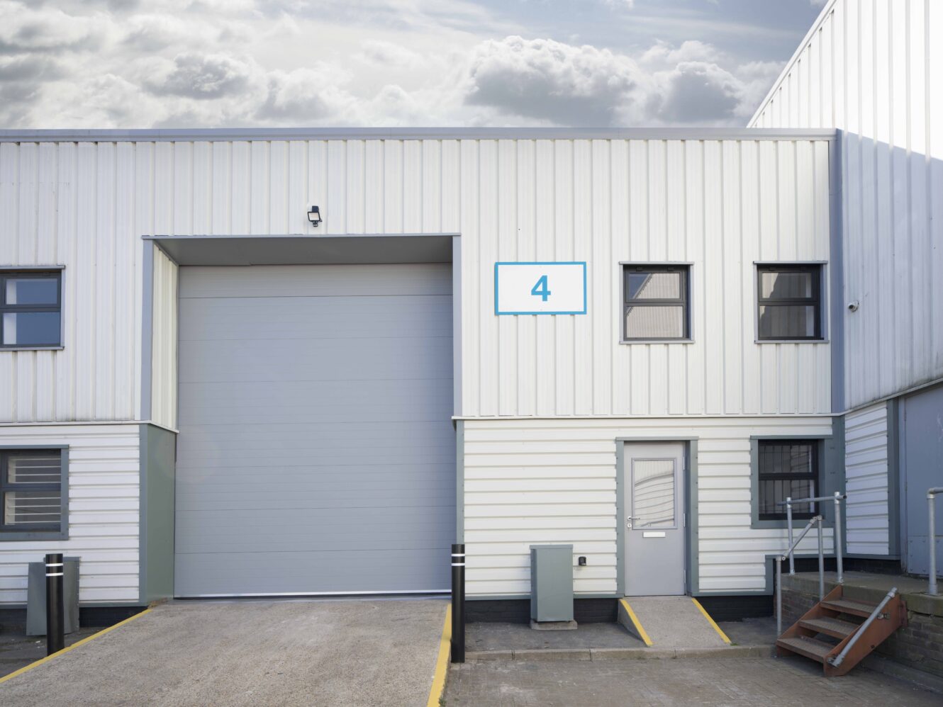 Exterior of a white industrial warehouse unit with a large closed garage door, labelled with a blue number 4 sign above the entrance.