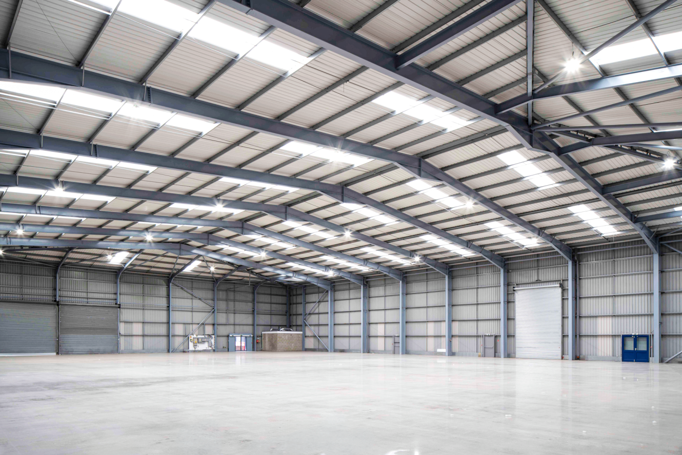 Spacious, empty warehouse with high metal ceiling, exposed beams, large shutter doors, and polished concrete floor, well-lit.