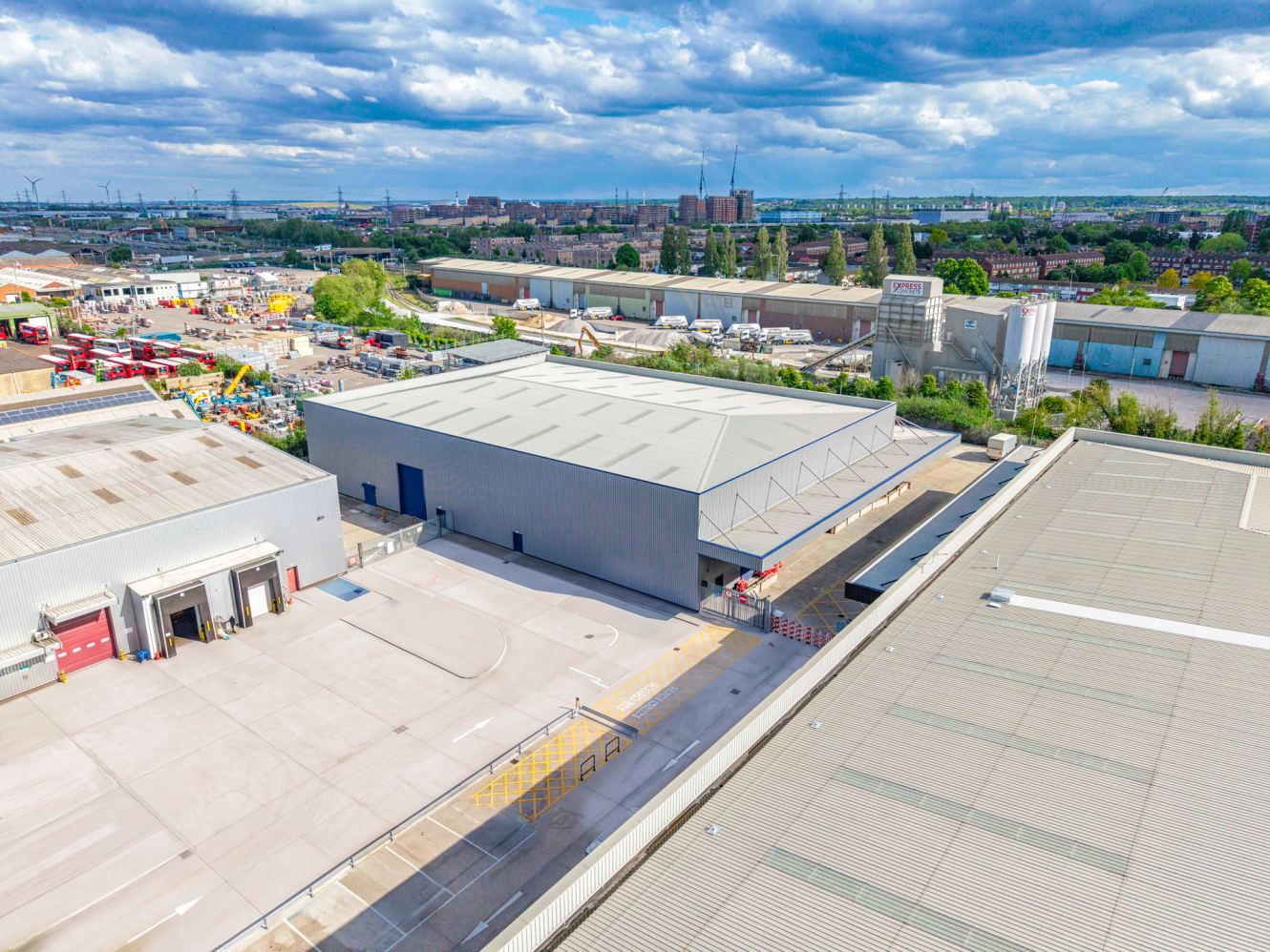 Aerial view of an industrial estate featuring large warehouses, paved car parks, equipment, and buildings under a partly cloudy sky.