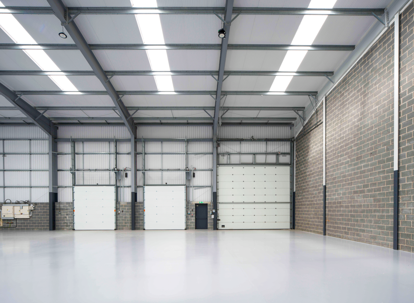 Interior of an empty industrial warehouse with polished concrete floor, brick walls, and large white loading bay doors.