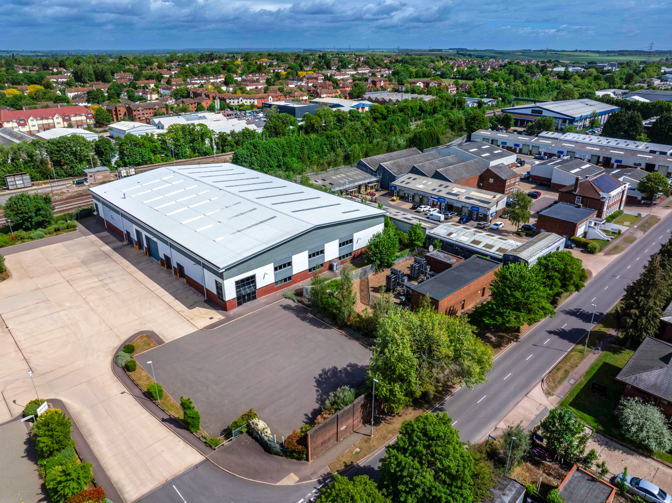 Aerial view of an industrial area with warehouses, car parks, and residential neighbourhoods surrounded by trees.