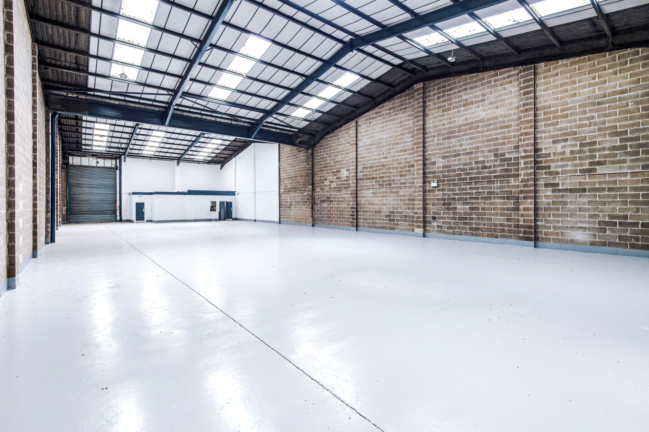 Interior of a spacious empty warehouse with brick walls, polished concrete floors, and skylights in the ceiling.