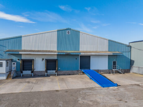 A large blue and white industrial warehouse with three loading bays, including one with a blue ramp, number 6 at the centre.