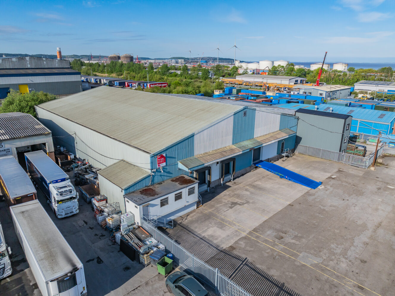 Aerial view of an industrial warehouse with loading bays, parked lorries, and storage containers in an urban area.