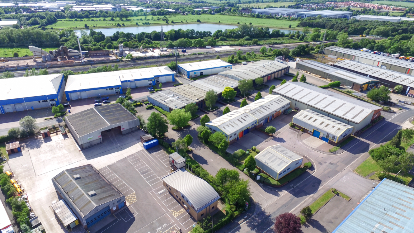 Aerial view of an industrial estate with warehouses, car parks, and greenery on a clear day.