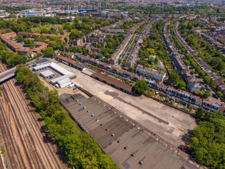 Aerial view of a neighbourhood with rows of houses, railway tracks on the left, and a large industrial building with an empty car park.