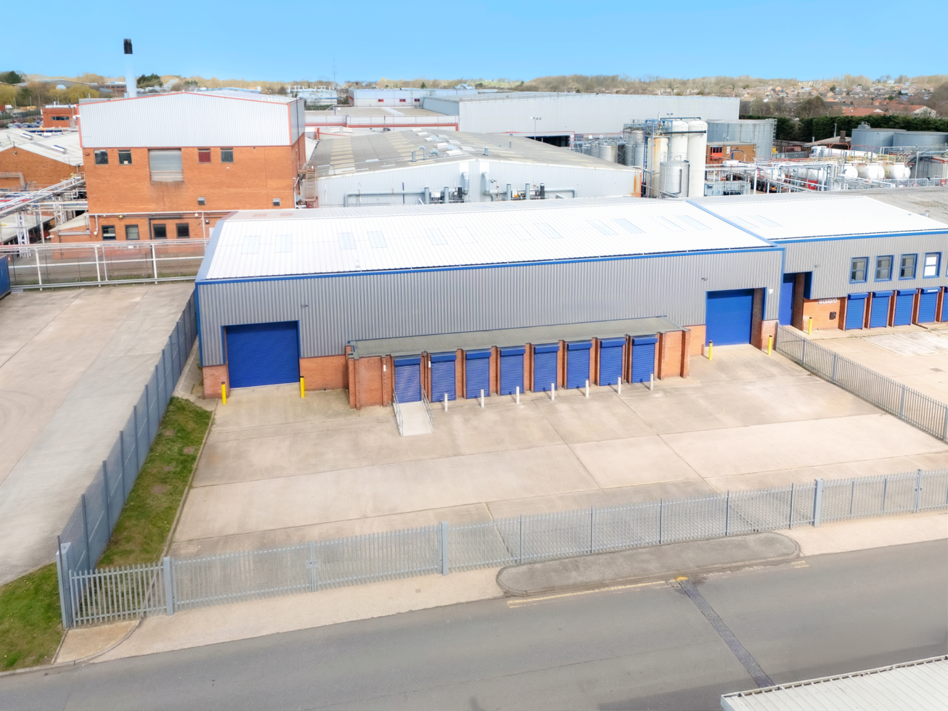 A large industrial building with blue doors and a fenced concrete yard, surrounded by warehouses and industrial facilities.