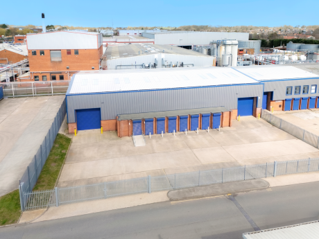 A large industrial building with blue doors and a fenced concrete yard, surrounded by warehouses and industrial facilities.