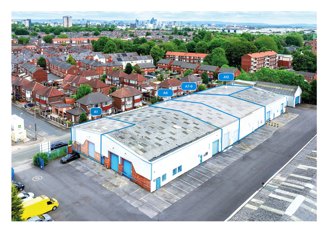 Aerial view of a large white industrial warehouse complex with labelled units, surrounded by houses and greenery.