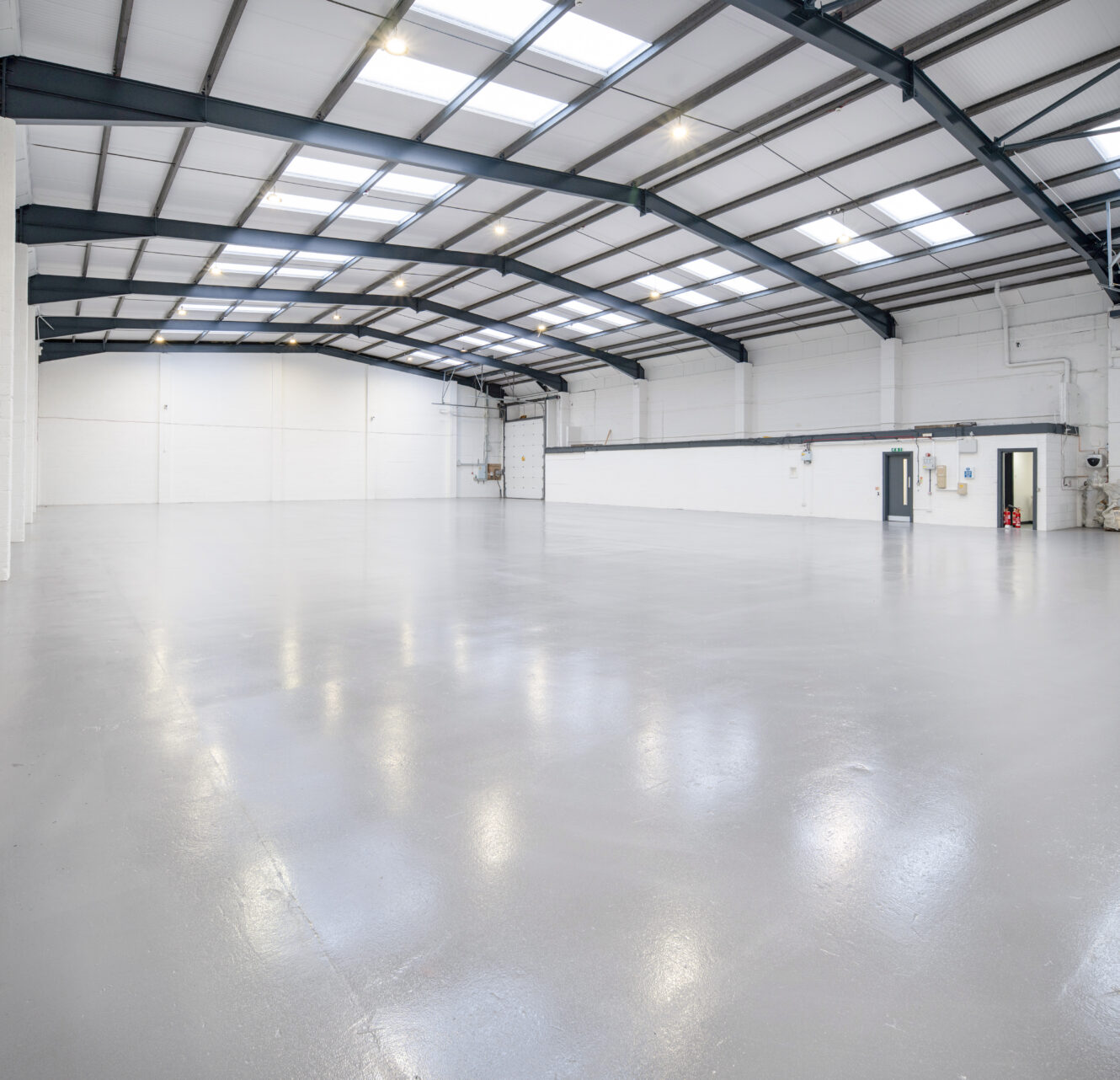Spacious warehouse interior with polished concrete floor, white walls, high ceiling, exposed steel beams, and bright lighting.