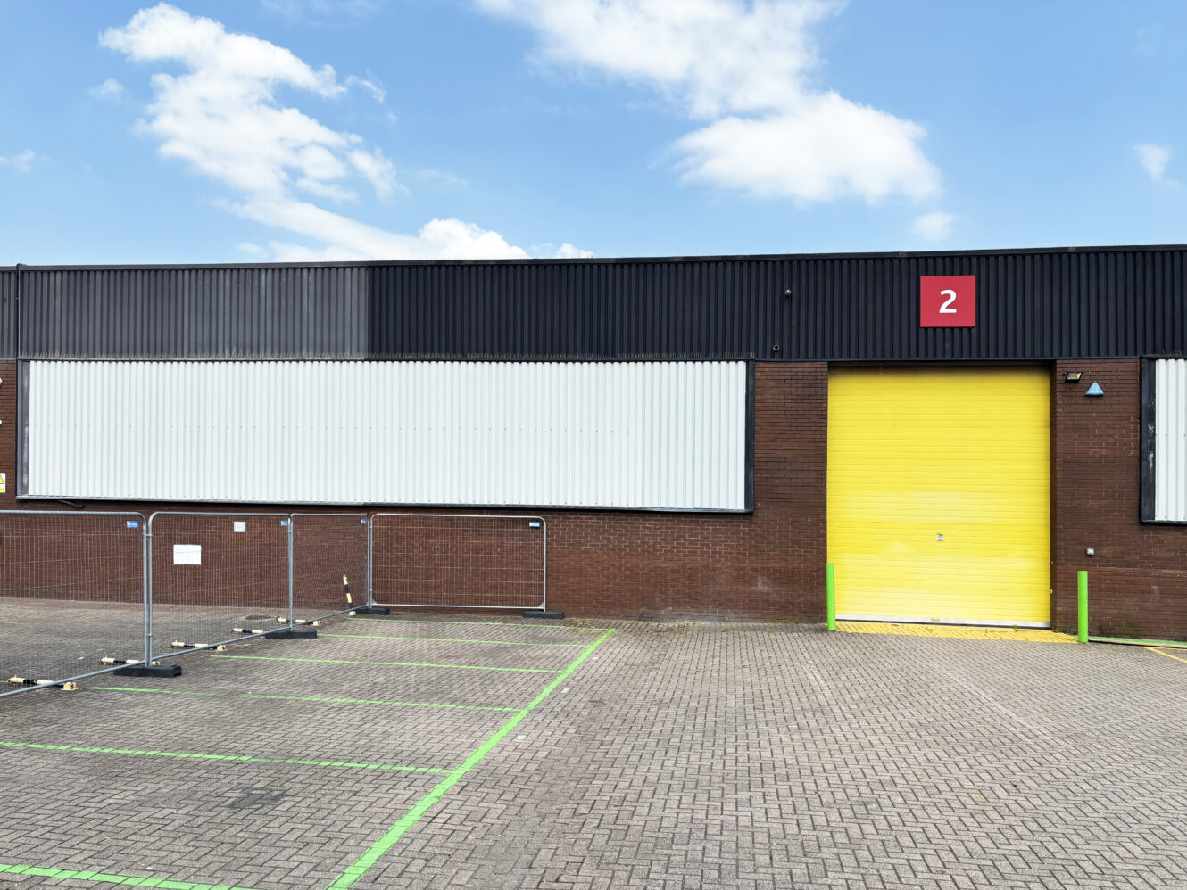 Industrial building with a yellow garage door, red sign showing the number 2, and empty parking spaces on the paved area in front.