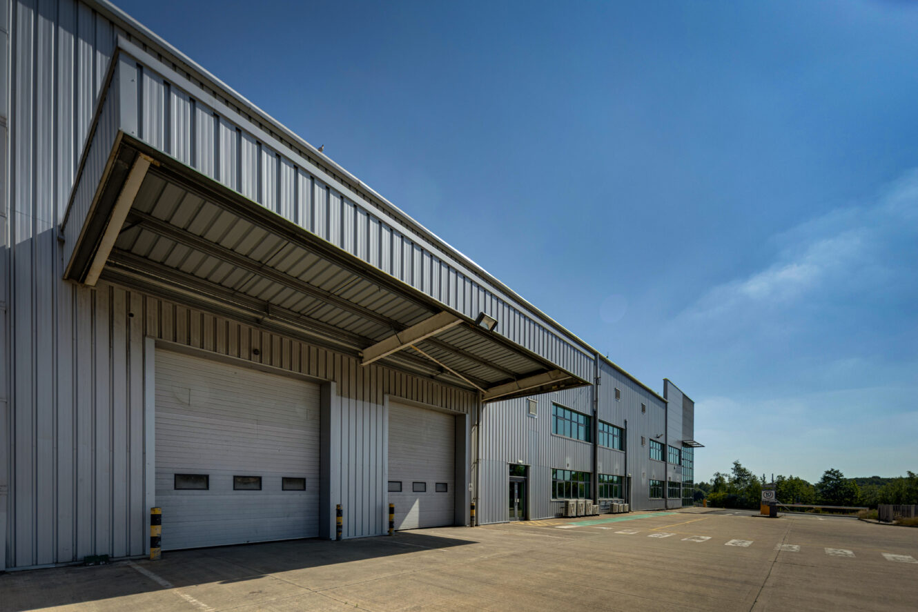 A large industrial warehouse with multiple loading bays, metal cladding, and overhead doors under a clear blue sky.