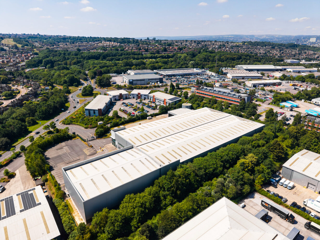Aerial view of an industrial estate with warehouses, office buildings, roads, and green spaces under a clear sky.