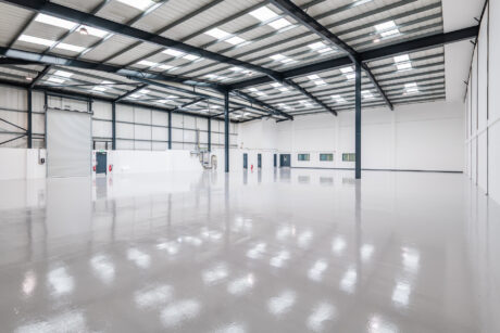 Interior of an empty, modern warehouse with polished concrete floors, high ceilings, exposed steel beams, and large windows.