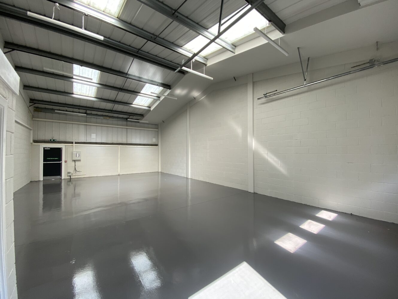 An empty industrial warehouse with white brick walls, high ceilings, skylights, and a polished concrete floor lit by natural light.