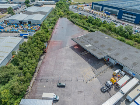 Aerial view of an industrial facility featuring warehouses, parked lorries, a car, and greenery surrounding the property.