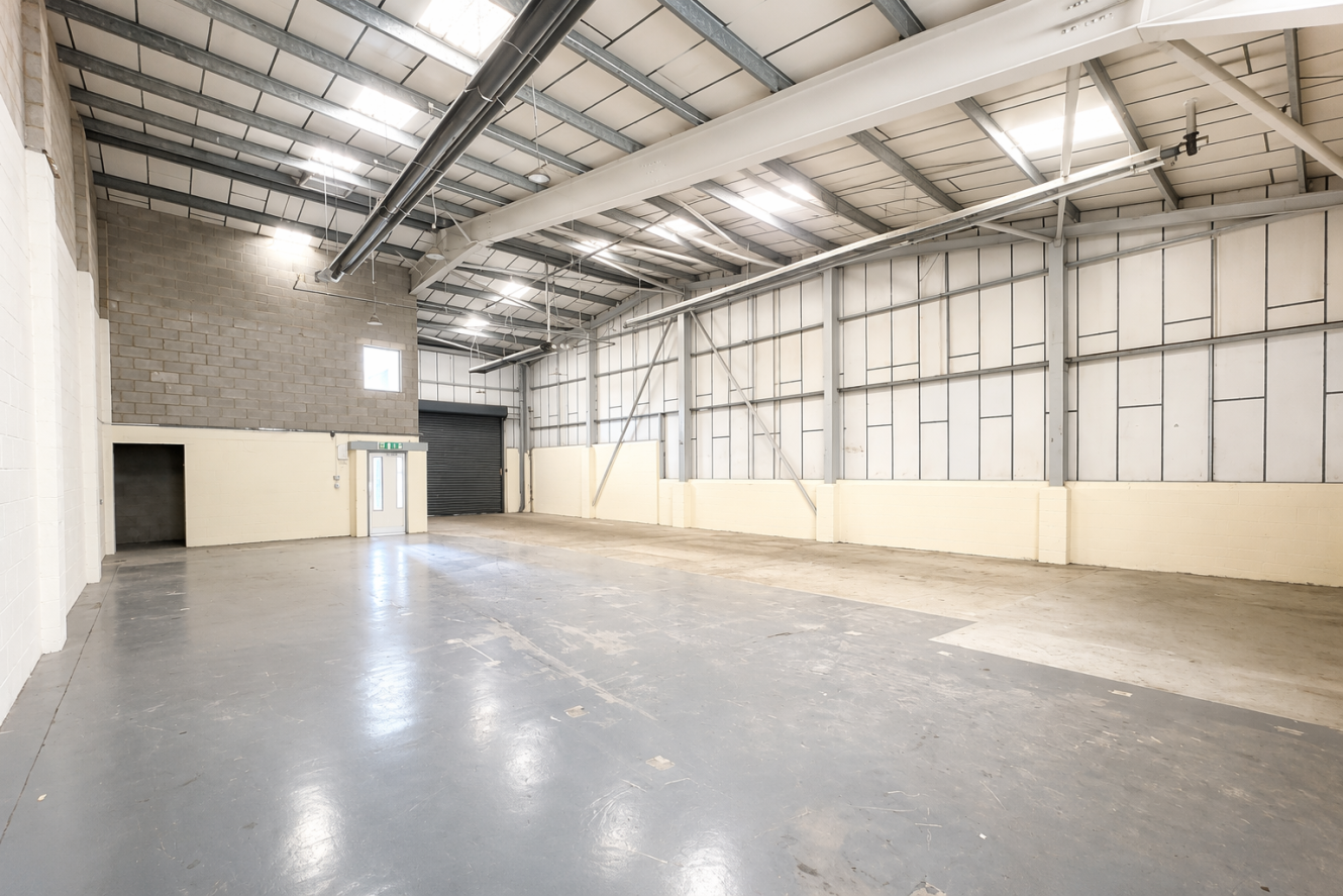 Large empty industrial warehouse with high ceiling, concrete floor, metal beams, brick walls, and both a regular door and a large loading bay door.